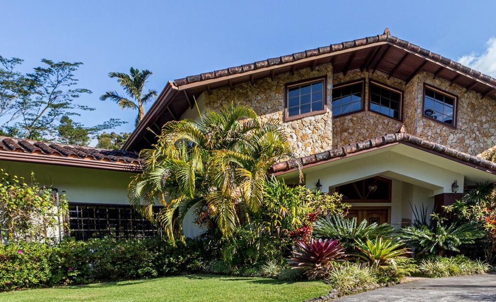 fachada delantera de casa con decoración de piedra y techo de teja y jardín con palmas